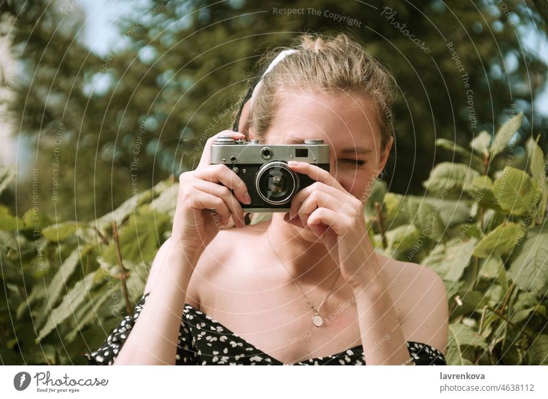 Junge blonde Frau hält fokussierende Vintage-Filmkamera im Freien Fotokamera Gerät Filmmaterial Fokus Hand Hobby Beteiligung Linse Lifestyle Person Fotograf