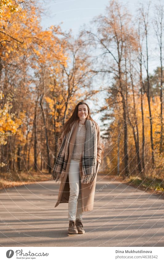 Junge schöne Frau mit langen Haaren in beigem Mantel spazieren im Herbst Park lächelnd glücklich Fröhlichkeit Lächeln elegant laufen Person Model Laubwerk