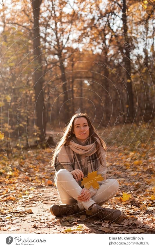 Junge Frau mit beige Schal und Jeans zu Fuß im Herbst Park bei Sonnenuntergang mit warmen Sonnenschein. Entspannende Momente in der Natur, Millennial Mädchen glücklich zu sein und lächelnd.