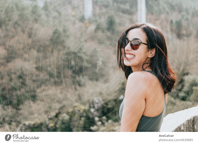 Eine junge Frau Reisende in sportlicher Kleidung und Sonnenbrille mit Blick von einer Klippe in den Wald, bewundern die Aussicht auf die Tierwelt. Gesundes Leben in der Natur junge Menschen Konzept.