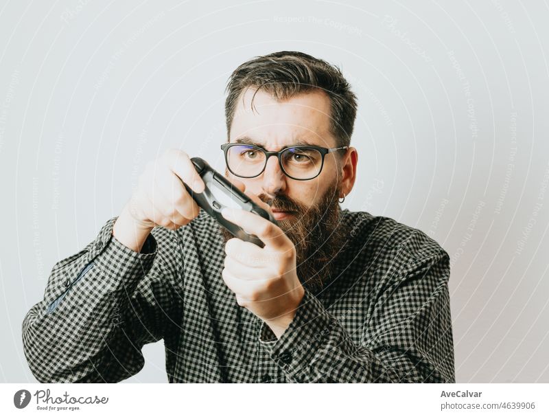 Junge gut aussehend bärtigen Mann mit Brille spielen mit einem Videospiel-Controller expresful Konzentrationen Gesichter lustig über isolierten weißen Hintergrund. Gaming Medium Alter Konzept. Kopieren Raum Konzept