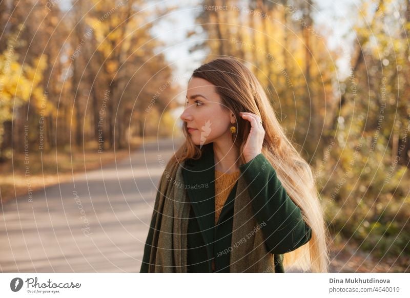 Schöne Frau in grünem Mantel und gelben Pullover im Herbst Park in der Nähe von Bäumen mit gelben Blättern bei Sonnenuntergang. Verbringen Sie Zeit in der Natur, um Frieden im Kopf, entspannende Momente und minfullness zu halten. Herbst-Stil und Mode, lässige Kleidung.