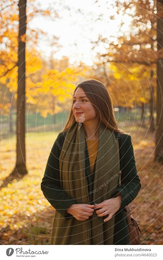Schöne Frau in grünem Mantel und gelben Pullover im Herbst Park in der Nähe von Bäumen mit gelben Blättern bei Sonnenuntergang. Verbringen Sie Zeit in der Natur, um Frieden im Kopf, entspannende Momente und minfullness zu halten. Herbst-Stil und Mode, lässige Kleidung.