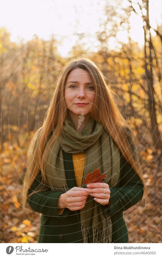 Schöne Frau mit langen Haaren in grünem Mantel steht im Herbst Park hält einen Herbst Ahornblatt. Stil, Mode und Kleidung. Tief in Gedanken im Herbst Wald in der Natur. Authentischer Lebensstil.