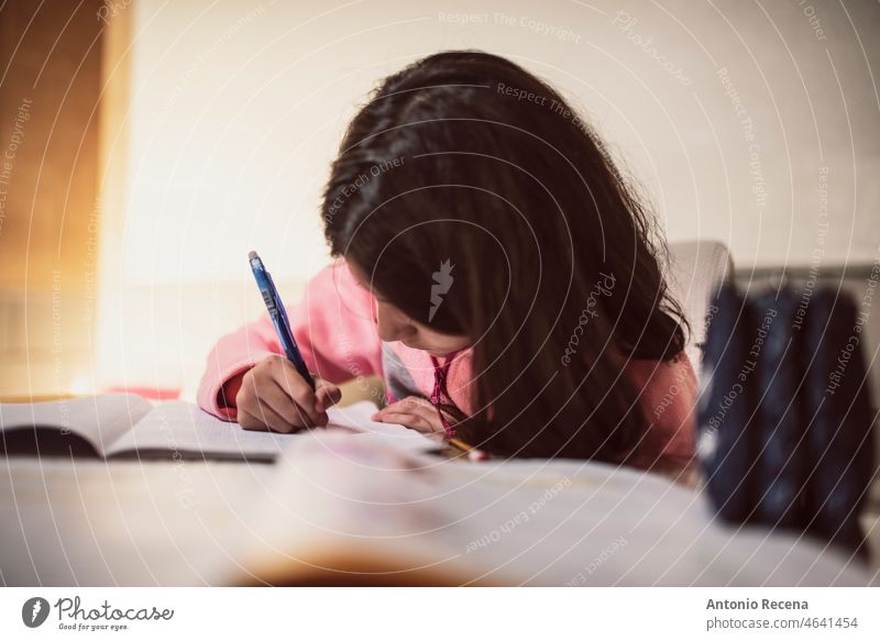 Ein Mädchen macht ihre Hausaufgaben zu Hause und schreibt konzentriert Kinder Hausarbeiten heimisch realistisch Trainingsanzug heimwärts Bücher Schüler