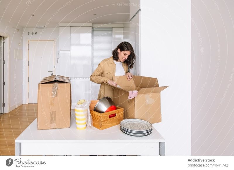 Frau beim Auspacken eines Kartons auf dem Boden auspacken Kasten Stock einziehen Appartement Küche Zugehörigkeit Tisch offen Paket neu Schachtel verweilen