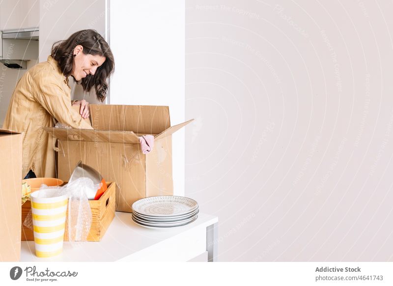 Frau beim Auspacken eines Kartons auf dem Boden auspacken Kasten Stock einziehen Appartement Küche Zugehörigkeit Tisch offen Paket neu Schachtel verweilen