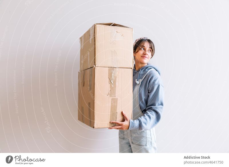 Positive Frau trägt Kartons Kasten führen verlegen Zugehörigkeit Lächeln Stapel Hypothek Hausbesitzerin positiv lässig Schachtel Optimist jung Paket einziehen