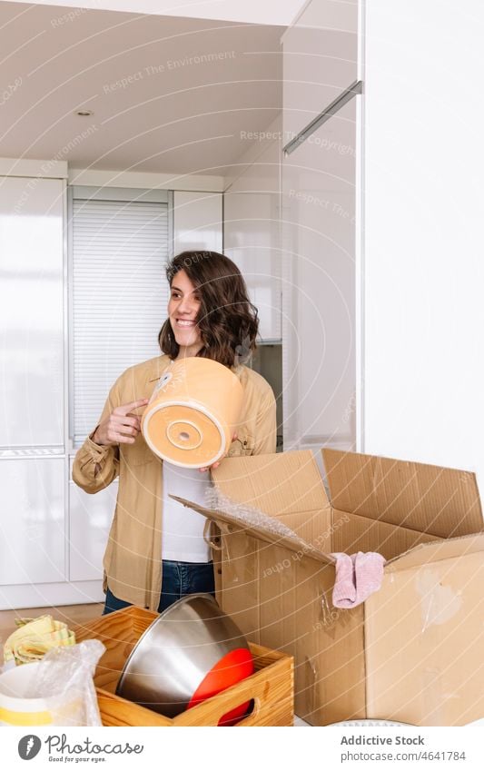 Frau beim Auspacken eines Kartons auf dem Boden auspacken Kasten Stock einziehen Appartement Küche Zugehörigkeit Tisch offen Paket neu Schachtel verweilen Topf