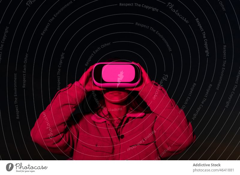 Frau, die nachts mit einer Brille virtuelle Realität betrachtet zuschauen VR Schutzbrille benutzend Nacht erkunden neonfarbig dunkel digital eintauchen