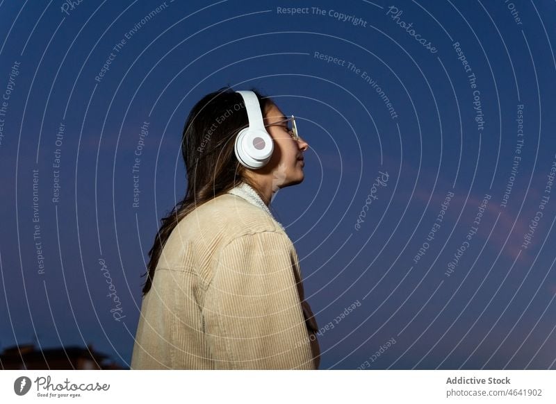 Anonyme Frau, die in der Abenddämmerung mit Kopfhörern Musik hört Drahtlos Glück Wiedergabeliste Sonnenuntergang zuhören Gesang Teenager genießen Freude positiv