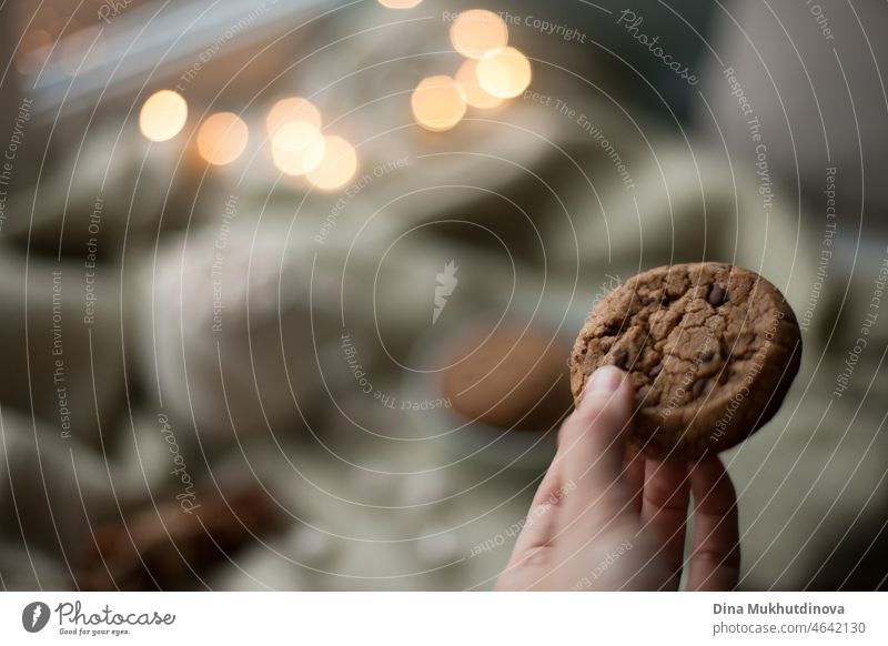 Hand hält einen hausgemachten Keks Nahaufnahme. Hausgemachte Chocolate Chip Cookies in gemütlichen Haus mit Lichtern Bokeh. Kopieren Sie Raum und Low-Key-Abend Hintergrund