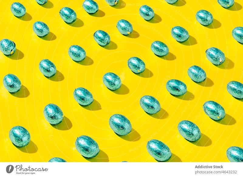 Muster aus grünen Schokoladeneiern aus Folie auf gelbem Hintergrund. Menschengruppe glänzend Kugel dreidimensional abstrakt Ball Konzept Design Ei Textur