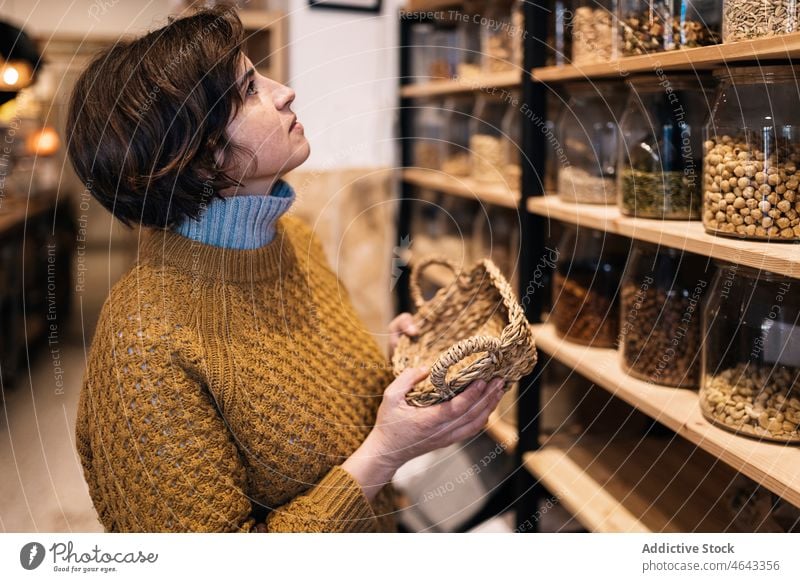 Frau mit Weidenkorb in den Händen in einem Öko-Laden stehend Korb umweltfreundlich keine Verschwendung Werkstatt Pullover Kunde wählen Regal Windstille