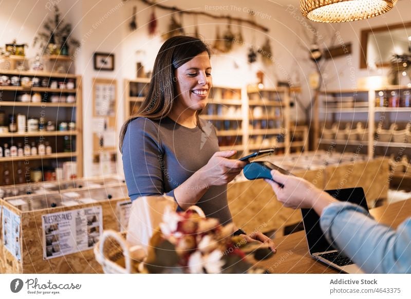 Schwangere Frau beim Bezahlen mit dem Smartphone in einem umweltfreundlichen Geschäft Frauen berührungslos Terminal Verkäufer Werkstatt Kunde Klient Kauf