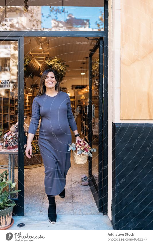 Schwangere Frau mit Korb in der Hand verlässt ein Geschäft Straße Lächeln heiter Großstadt Werkstatt umweltfreundlich schwanger positiv pränatal lange Haare