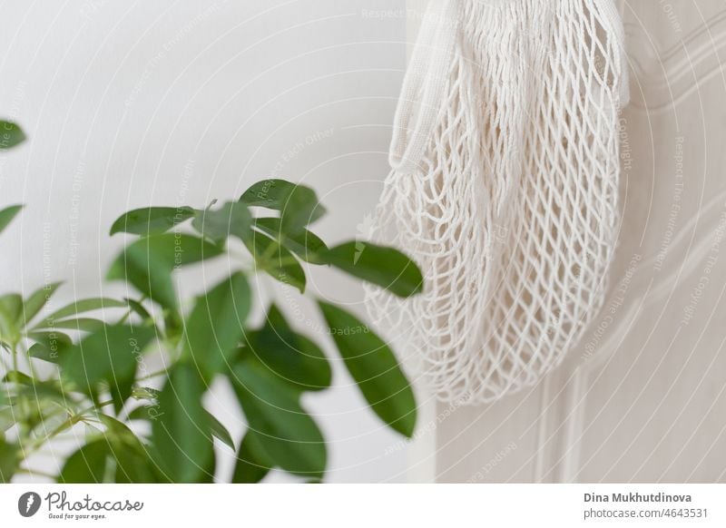 Öko-Netz-Tragetasche für Lebensmitteleinkäufe hängt am Türknauf zu Hause in der Nähe von grünen Blättern auf Zimmerpflanze Lebensmittelgeschäft kaufen Tasche