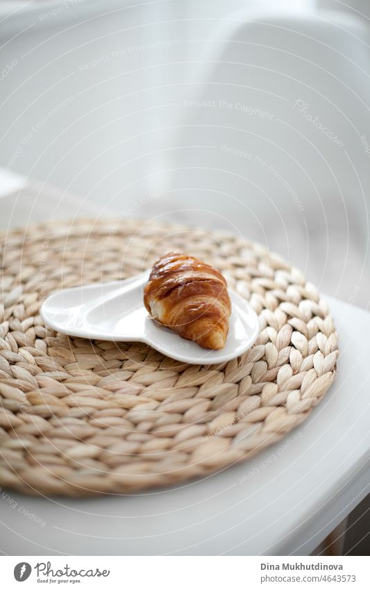 Frisch gebackenes französisches Croissant auf einem beigen Tischset auf weißem Tisch zu Hause am Morgen, im Hotelzimmer oder im Café keine Menschen Frühstück