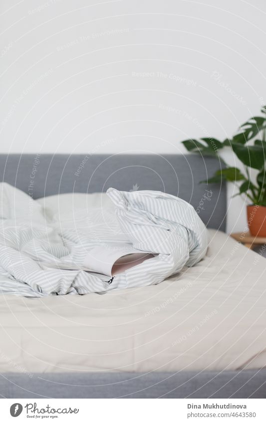 ein aufgeschlagenes Buch liegt auf dem Bett in einer gemütlichen Wohnung im minimalistischen skandinavischen Stil in neutralen hellen Farben mit einer grünen Pflanze