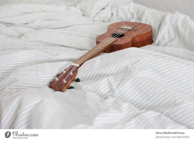 Ukulele guiutar auf dem Bett liegend auf der weiß gestreiften Decke. Hobby und Musik spielen in gemütlichen Haus. Minimalismus skandinavischen Stil zu Hause.