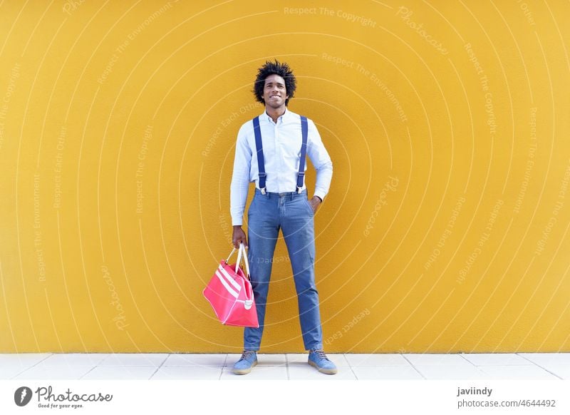 Stilvoller schwarzer Mann an gelber Wand stehend smart lässig Großstadt Lächeln heiter Outfit gut gekleidet Straße Glück männlich Afroamerikaner ethnisch