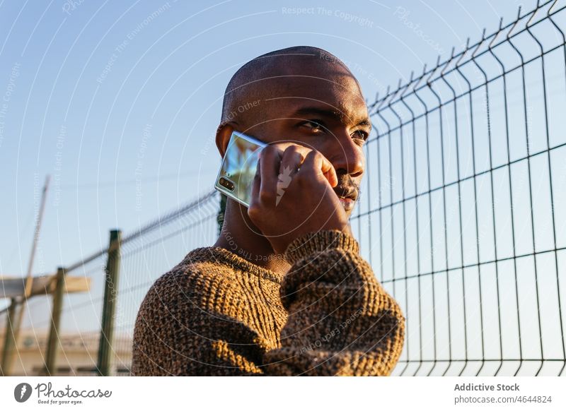 Schwarzer Mann spricht mit Smartphone in der Nähe des Zauns Telefonanruf Gespräch diskutieren Straße Anschluss Kommunizieren Großstadt Barriere Metall Fechten