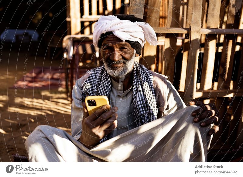 Älterer ethnischer Mann mit Smartphone auf der Straße authentisch lokal Kultur einheimisch benutzend Browsen Senior Funktelefon heimatlich zuschauen älter