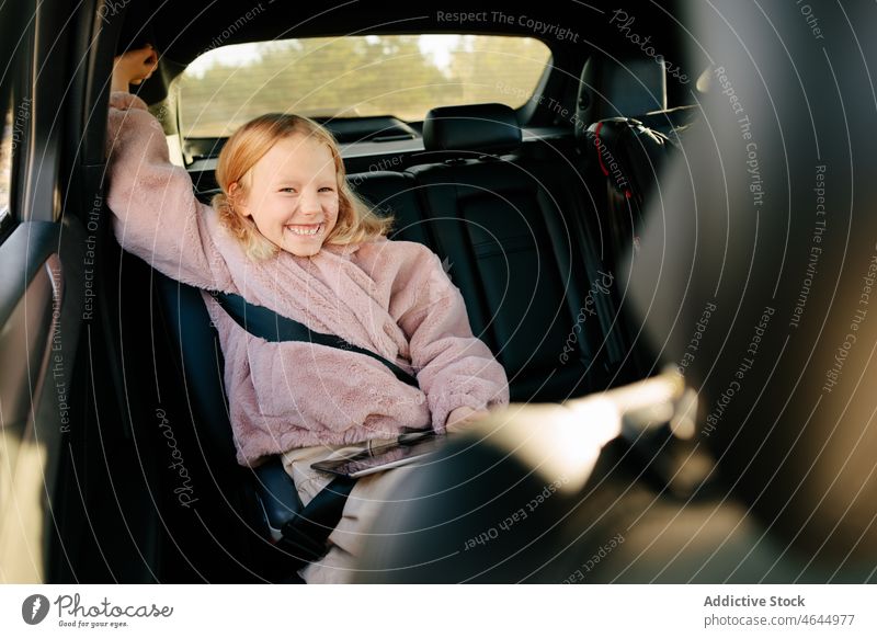 Fröhliches Mädchen sitzt im Auto Kind PKW Automobil Passagier Rücksitz Mitfahrgelegenheit Ausflug Arbeitsweg Spaß haben Tablette Sitz modern Glück Gerät