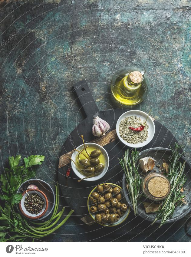 Lebensmittel Hintergrund mit Oliven, Olivenöl, Kapern, Salz, Knoblauch und Rosmarin auf rustikalen Küchentisch Lebensmittelhintergrund Kapriolen Tisch