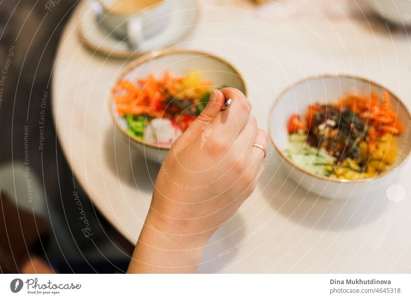 Essen poke bowl im Restaurant. Bunte hawaiianische Gericht poke Schüssel von frischem Gemüse und Fisch in Scheiben geschnitten gemacht. Hand hält eine Gabel Nahaufnahme. Tasting traditionellen exotischen hawaiianischen Essen Mahlzeit.