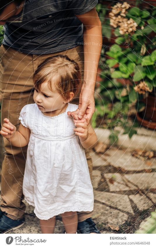 Kleines blondes Mädchen hält die Hand ihres Vaters im Garten. Kind schaut neugierig. Kindheit und Familie Konzept. Papa Kinderbetreuung Papi Händchenhalten