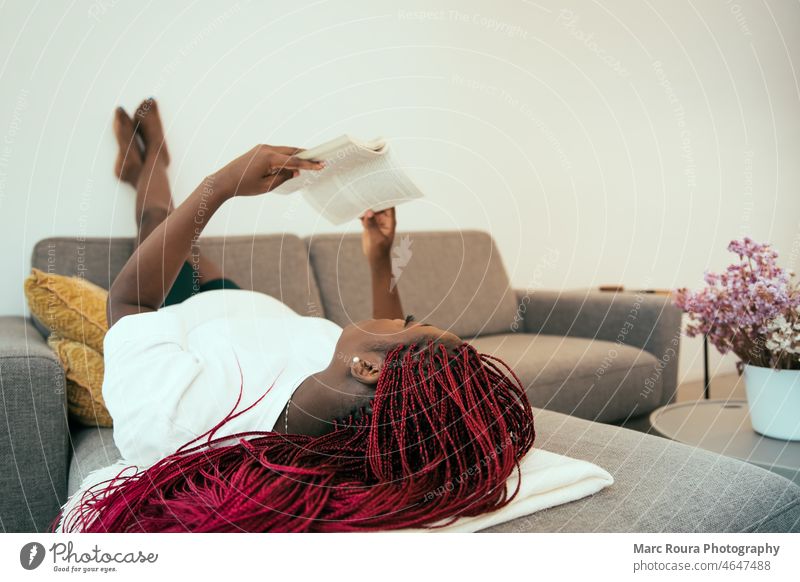 Schwarze Frau liegt auf dem Sofa und liest ein Buch mit den Füßen an der Wand Erwachsener Afrikanisch attraktiv Hintergrund schön Schönheit schwarze Frau heiter
