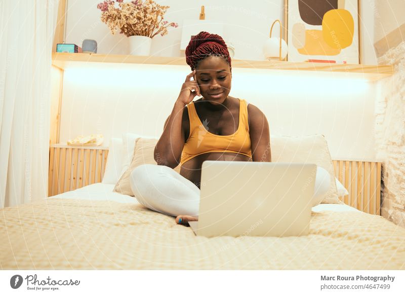 schwangere schwarze Frau, die sich zu Hause auf dem Bett mit einem Laptop entspannt Afrikanisch Appartement Schlafzimmer Bauch Business Pflege Komfort Computer