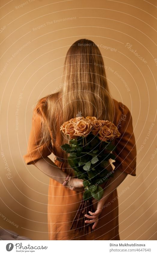 Frau in braunem Kleid hält braune Rosen auf beige-braunem Hintergrund, florales Konzeptbild Kaffee erdig beiger Hintergrund Monochrom minimalistisch lange Haare
