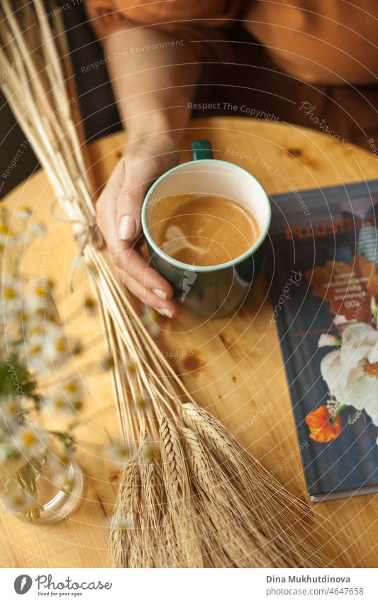 Kaffeetrinken aus einem grünen Becher in einem Café, auf einem Holztisch mit einem Buch und einem Weizenstrauß hübsch Frau Porträt Erholung junger Erwachsener