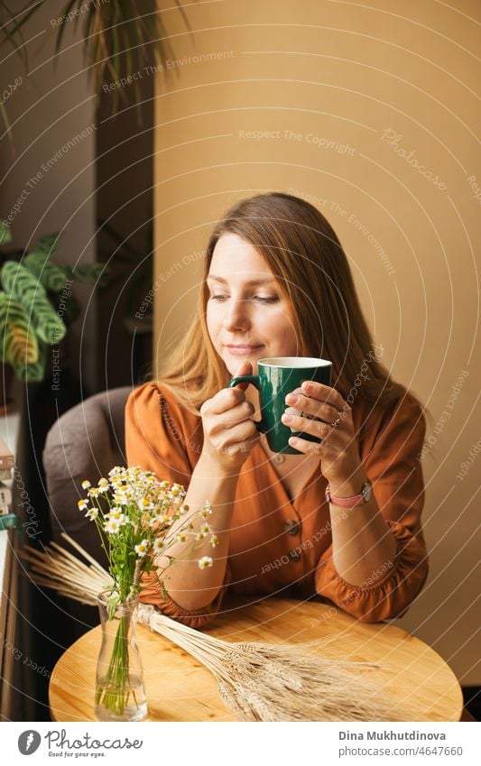 Schöne Frau in braunem Kleid im Café trinkt Kaffee aus grüner Tasse, ist ruhig, denkt nach und entspannt sich Person trinken hübsch Porträt jung Erholung