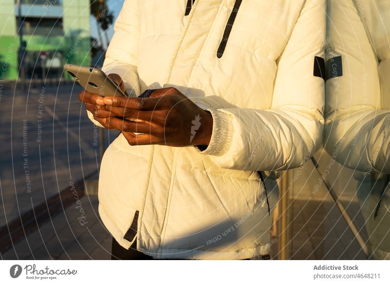 Anonymer afroamerikanischer Mann, der in der Nähe einer gläsernen Gebäudewand telefoniert Smartphone Funktelefon benutzend Browsen Telefon Texten Glaswand