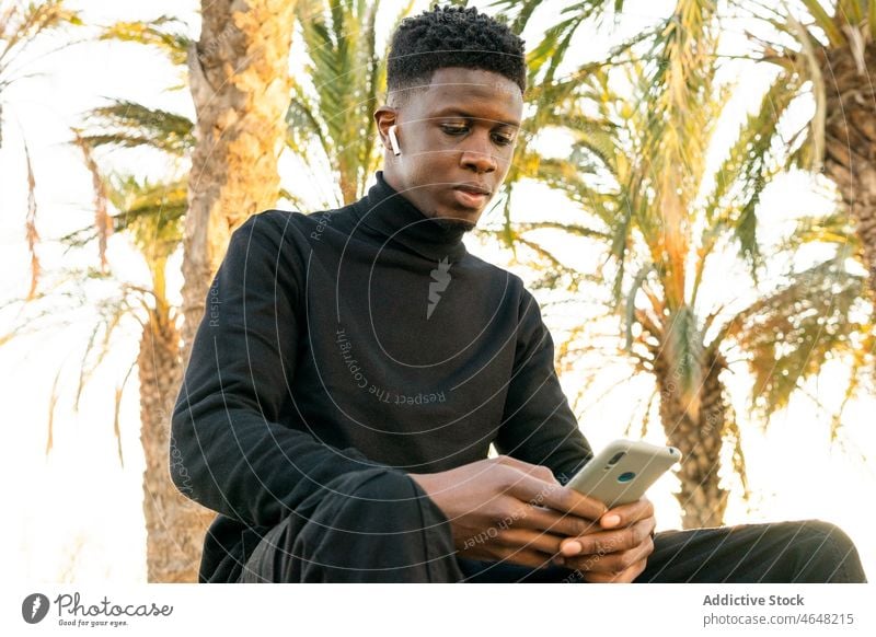 Crop Afroamerikanischer Mann beim Telefonieren im Park Smartphone Funktelefon benutzend Browsen Bank Texten Kälte männlich schwarz Textnachricht Surfen