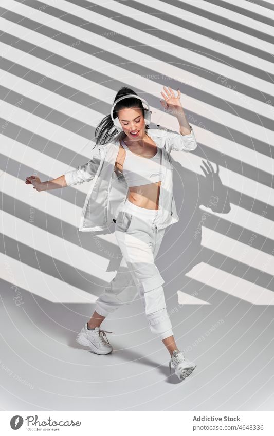 Junge Frau tanzt Hip-Hop im gestreiften Studio Tänzer Tanzen Freestyle Kopfhörer Hobby Schatten Streifen ausführen zuhören Glück Probe Musik Fähigkeit Gesang