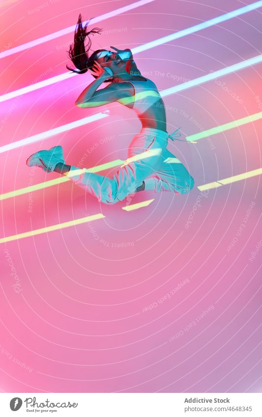 Energetische Frau hört Musik und springt im Studio zuhören Kopfhörer springen Glück neonfarbig Streifen Tanzen aktiv cool ausführen Hip-Hop Inspiration