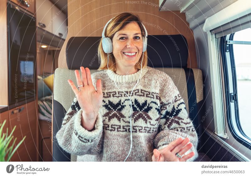 Glückliche Frau winkt per Videoanruf aus ihrem Wohnmobil schauende Kamera Anruf winkend Videokonferenz Kopfhörer Fernarbeit Kleintransporter reisen Lächeln