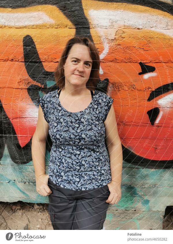 In Schlumperklamotten steht sie vor einer kreativ, mit Graffiti gestalteten Wand eines Lost Place. Frau feminin Mensch Erwachsene Farbfoto Außenaufnahme Shirt