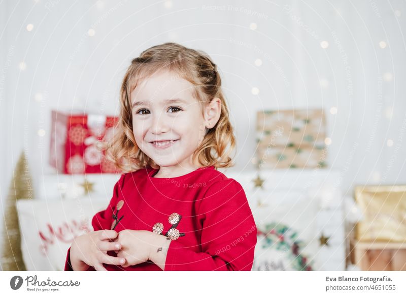 glücklich niedlichen kleinen Mädchen zu Hause tragen rote Weihnachtskleid zu Hause über Weihnachtsdekoration. Urlaub Konzept Glück Weihnachten heimwärts Kind