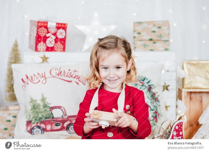glückliches kleines Mädchen zu Hause hält Spielzeugkamera tragen rote Weihnachtskleid zu Hause über Weihnachtsdekoration. Urlaub Konzept Glück Weihnachten