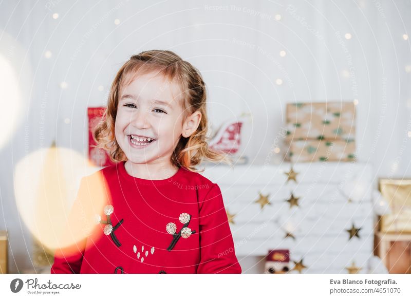 Porträt von glücklichen kleinen Mädchen zu Hause tragen rote Weihnachtskleid zu Hause über Weihnachtsdekoration. Urlaub Konzept Glück Weihnachten heimwärts Kind