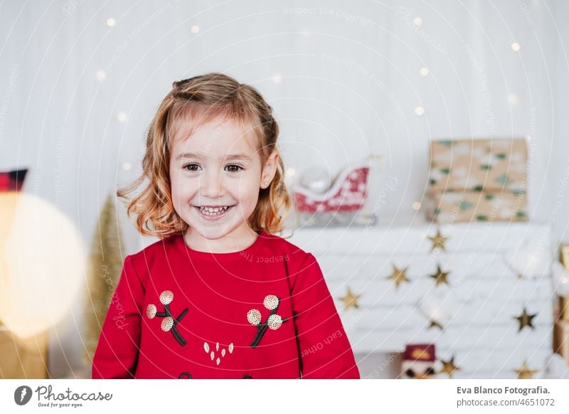 Porträt von lächelnden kleinen Mädchen zu Hause tragen rote Weihnachtskleid zu Hause über Weihnachtsdekoration. Urlaub Konzept Glück Weihnachten heimwärts Kind