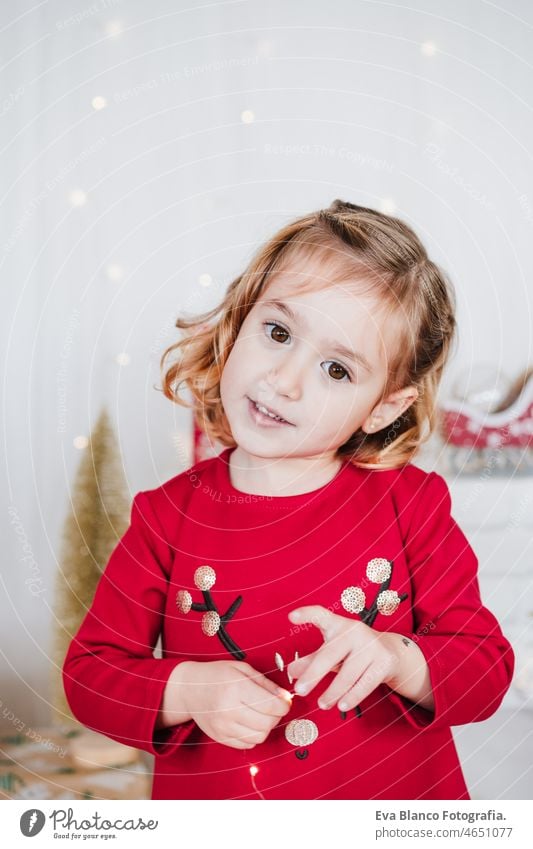 Porträt von niedlichen kleinen Mädchen zu Hause tragen rote Weihnachtskleid zu Hause über Weihnachtsdekoration. Urlaub Konzept Glück Weihnachten heimwärts Kind