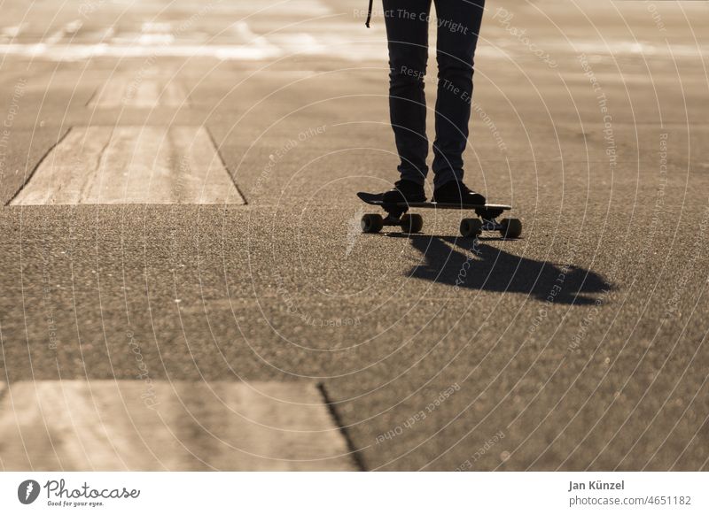 Skateboader auf Asphalt Skateboarding Skateboarderin Silhouette Gegenlicht Textfreiraum links Tiefenschärfe Tiefenunschärfe Monochrom Sonnenlicht Warmes Licht