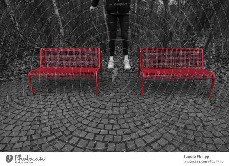 Color-Key-Effekt Foto, Mädchen springt zwischen zwei roten Bänken Beine springen Bewegung Aussenaufnahme Farbkontrast schwarz Bäume monocrom Fuß Mensch