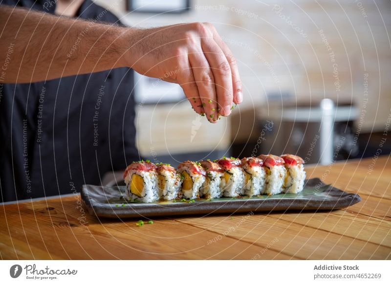 Anonymer Mann, der Kräuter auf Sushi-Rollen streut Küchenchef rollen Thunfisch Japanisch bestäuben Asiatische Küche dienen Meeresfrüchte Kraut kulinarisch